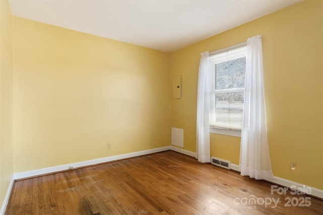 unfurnished room featuring hardwood / wood-style flooring, baseboards, and visible vents