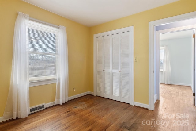 unfurnished bedroom with a closet, visible vents, baseboards, and wood finished floors