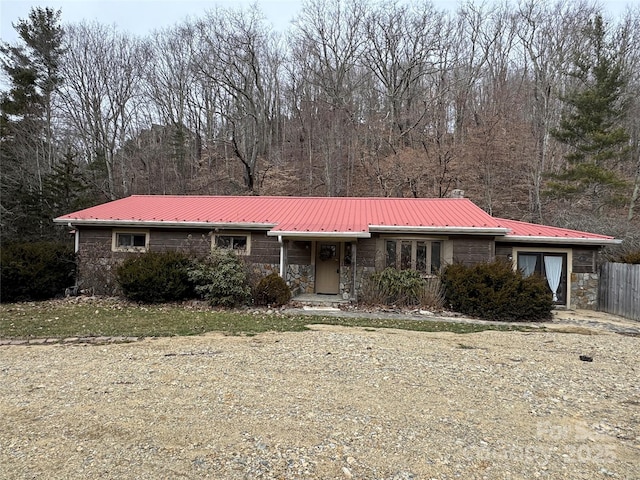 view of front facade featuring a forest view, metal roof, and stone siding