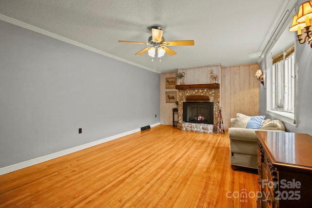 living area with ceiling fan, baseboards, light wood-type flooring, ornamental molding, and a stone fireplace