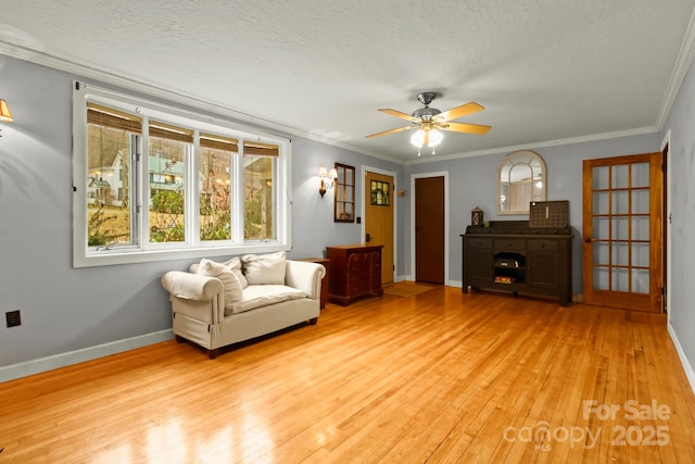 living area with a textured ceiling, light wood-type flooring, baseboards, and ornamental molding