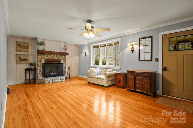 living area featuring crown molding, hardwood / wood-style floors, a stone fireplace, a textured ceiling, and a ceiling fan