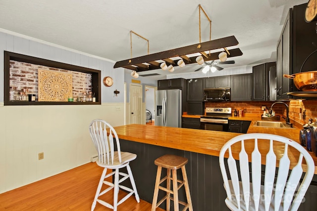 kitchen with a peninsula, a sink, stainless steel appliances, light wood-style floors, and wood counters