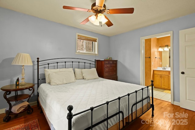 bedroom featuring light wood finished floors, ceiling fan, ensuite bath, and baseboards