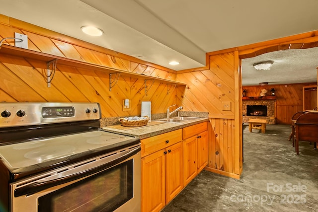 kitchen with electric range, a sink, open floor plan, wooden walls, and a fireplace