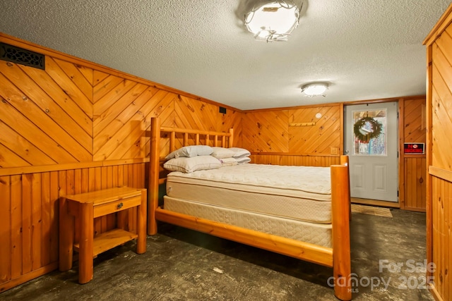 bedroom featuring a textured ceiling, concrete flooring, and wood walls