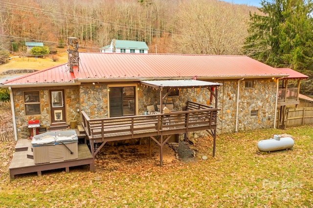 back of property with a deck, stone siding, metal roof, a chimney, and a hot tub