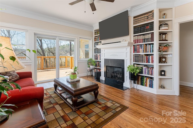 living room featuring wood finished floors, a fireplace, crown molding, baseboards, and ceiling fan