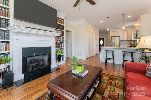 living room featuring light wood finished floors, ceiling fan, ornamental molding, recessed lighting, and a tile fireplace