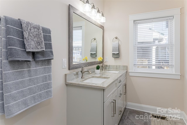 full bath featuring double vanity, baseboards, and a sink