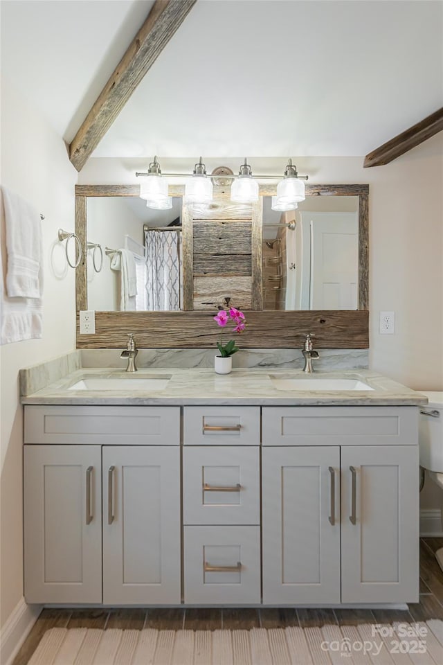 bathroom featuring double vanity, beamed ceiling, toilet, and a sink