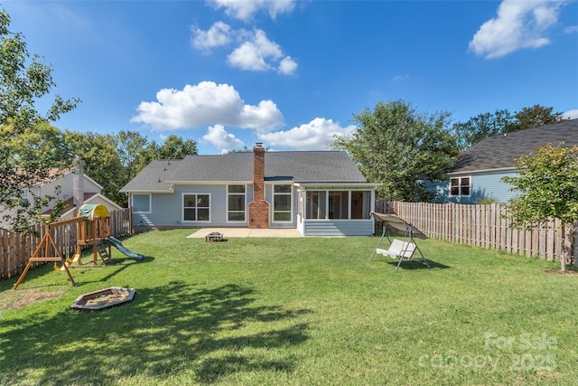 rear view of house with a playground, a sunroom, a chimney, a yard, and a fenced backyard