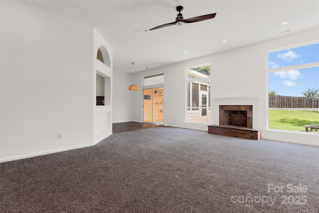 unfurnished living room with baseboards, a brick fireplace, ceiling fan, and dark carpet