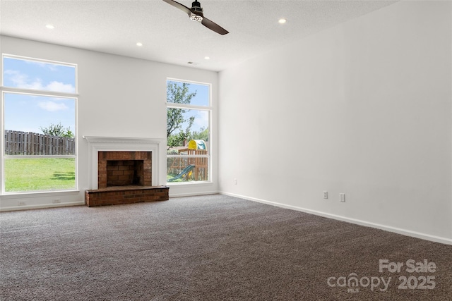 unfurnished living room with a brick fireplace, baseboards, carpet flooring, a textured ceiling, and a ceiling fan