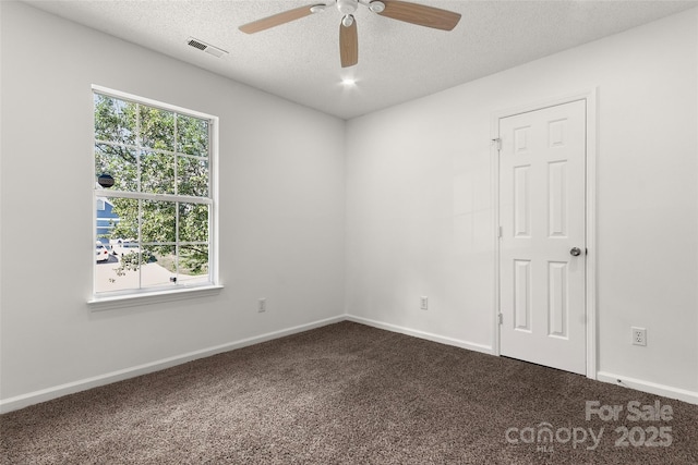 spare room featuring visible vents, dark carpet, a textured ceiling, and a ceiling fan