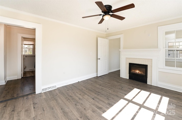 unfurnished living room featuring crown molding, wood finished floors, a warm lit fireplace, and ceiling fan