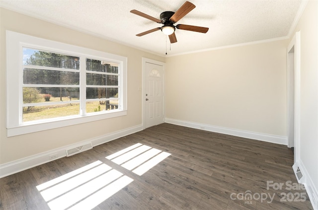 empty room with a ceiling fan, baseboards, dark wood finished floors, a textured ceiling, and crown molding