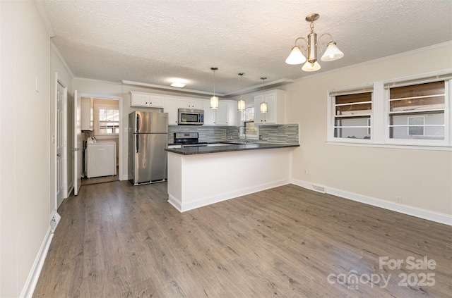 kitchen with dark wood finished floors, stainless steel appliances, a peninsula, white cabinets, and a chandelier