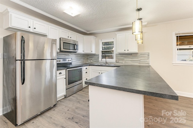 kitchen featuring ornamental molding, a sink, dark countertops, appliances with stainless steel finishes, and a peninsula