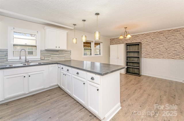 kitchen with a wainscoted wall, a peninsula, a sink, dark countertops, and light wood-type flooring