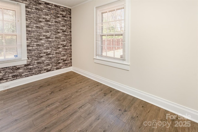 spare room with baseboards, wood finished floors, brick wall, and ornamental molding