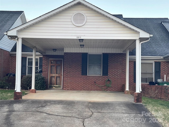 view of front of house with an attached carport, brick siding, and a shingled roof