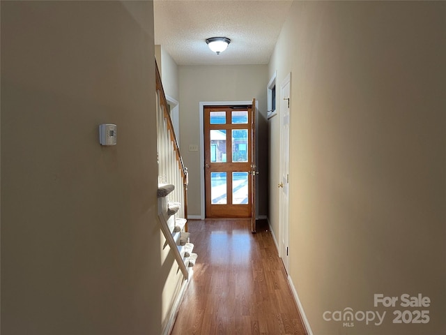 entryway featuring stairway, wood finished floors, baseboards, and a textured ceiling