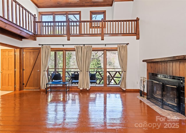 living room featuring hardwood / wood-style floors, baseboards, a fireplace with flush hearth, and a towering ceiling