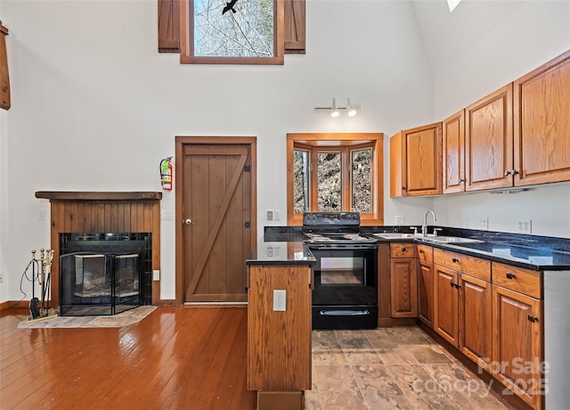 kitchen with a fireplace with flush hearth, high vaulted ceiling, a sink, black range with electric cooktop, and brown cabinetry