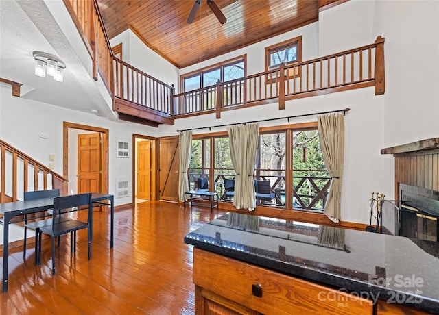 kitchen featuring baseboards, a high ceiling, hardwood / wood-style flooring, wood ceiling, and a glass covered fireplace