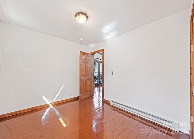 empty room featuring hardwood / wood-style floors, baseboards, and baseboard heating