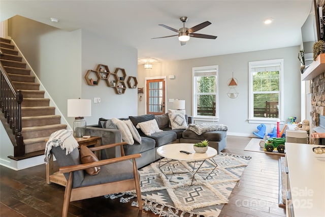 living area featuring dark wood finished floors, a stone fireplace, stairway, and baseboards