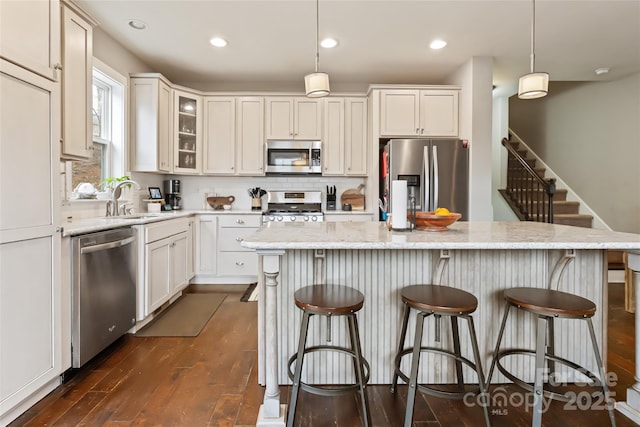 kitchen featuring tasteful backsplash, dark wood-type flooring, decorative light fixtures, stainless steel appliances, and a sink