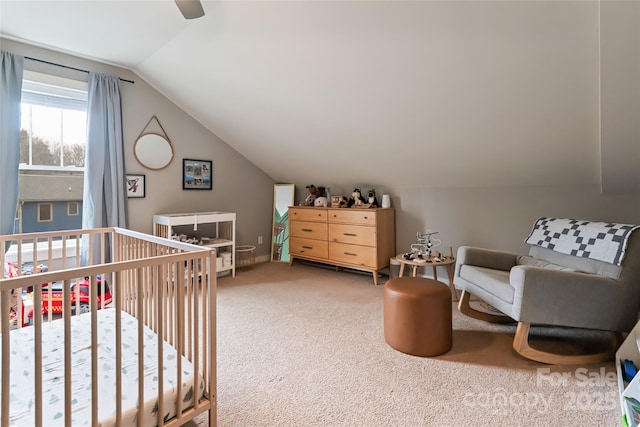 carpeted bedroom with a crib, lofted ceiling, and ceiling fan