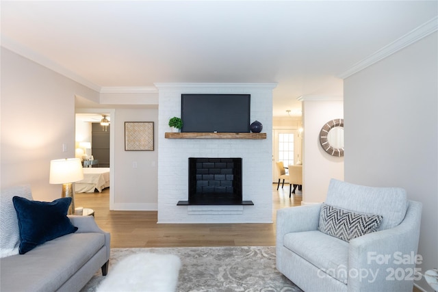 living area featuring a brick fireplace, wood finished floors, baseboards, and ornamental molding