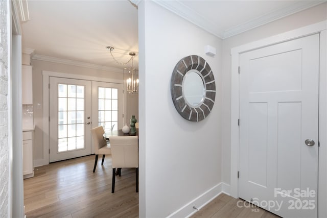 foyer entrance with a chandelier, baseboards, crown molding, and light wood-style floors