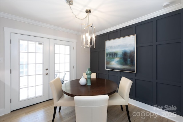 dining room with ornamental molding, french doors, an inviting chandelier, light wood-style floors, and a decorative wall