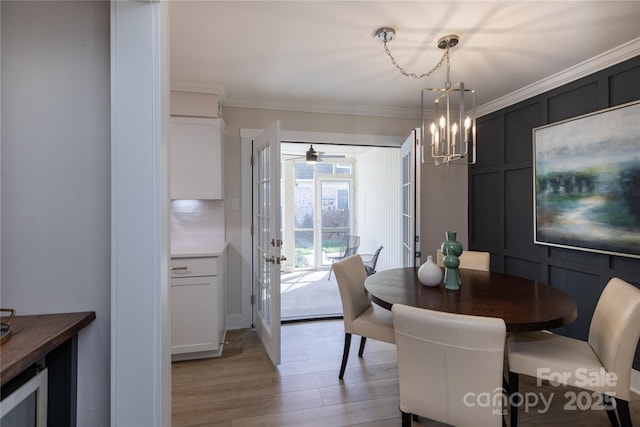 dining room featuring light wood finished floors, an inviting chandelier, crown molding, and a decorative wall