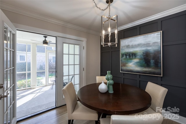 dining space with a chandelier, wood finished floors, crown molding, and a decorative wall