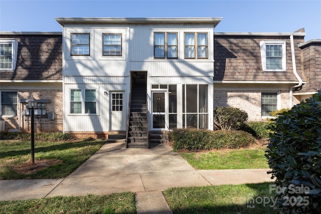 multi unit property with mansard roof, brick siding, entry steps, and a shingled roof