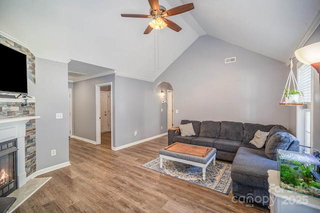 living room featuring visible vents, lofted ceiling, a stone fireplace, wood finished floors, and arched walkways