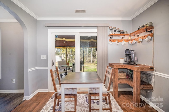 dining area featuring wood finished floors, baseboards, visible vents, arched walkways, and ornamental molding