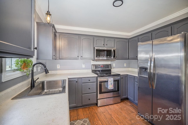 kitchen featuring wood finished floors, a sink, ornamental molding, light countertops, and stainless steel appliances