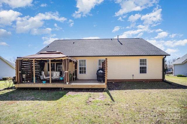 rear view of property featuring a gazebo, a wooden deck, a yard, and roof with shingles