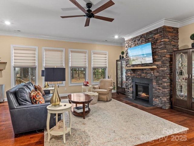 living area featuring dark wood finished floors, crown molding, a stone fireplace, and ceiling fan