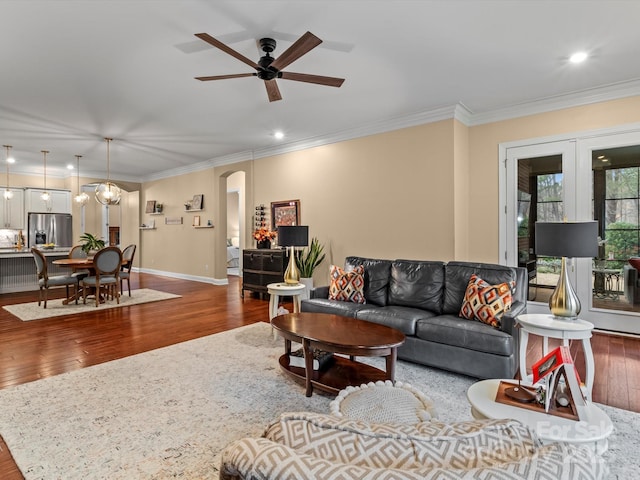 living room featuring hardwood / wood-style floors, a ceiling fan, baseboards, arched walkways, and ornamental molding