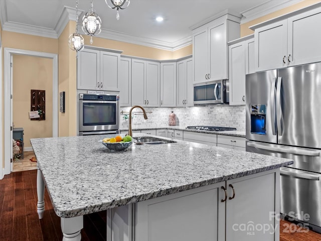 kitchen featuring an island with sink, ornamental molding, a sink, backsplash, and stainless steel appliances