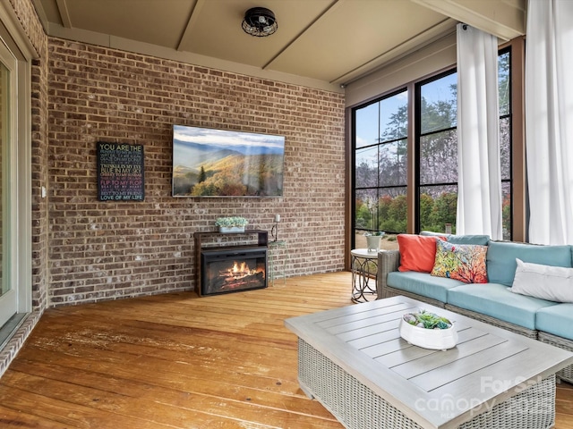 living room featuring a glass covered fireplace, brick wall, and hardwood / wood-style floors