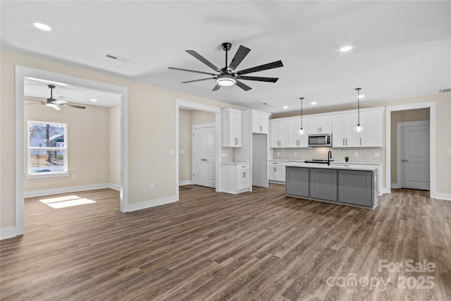 kitchen featuring visible vents, stainless steel microwave, white cabinets, light countertops, and decorative backsplash