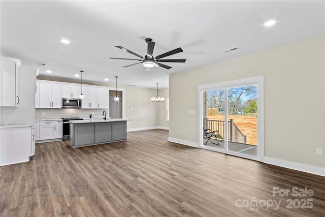 kitchen featuring dark wood finished floors, stainless steel appliances, light countertops, ceiling fan with notable chandelier, and tasteful backsplash